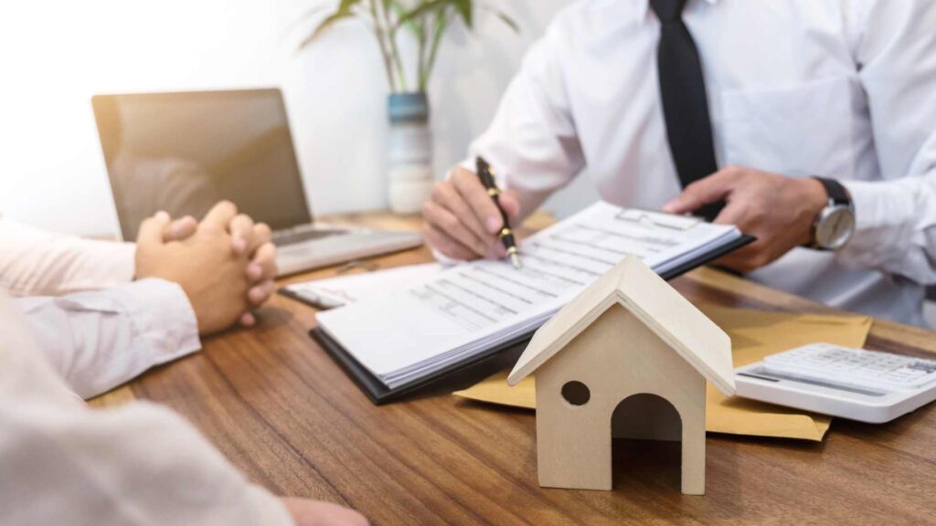 property manager showing a rental contract to a tenant with a house figurine on their desk