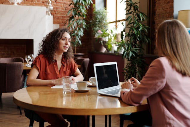 two-people-sitting-at-a-table-with-cups-of-coffee-and-a-laptop-having-a-conversation